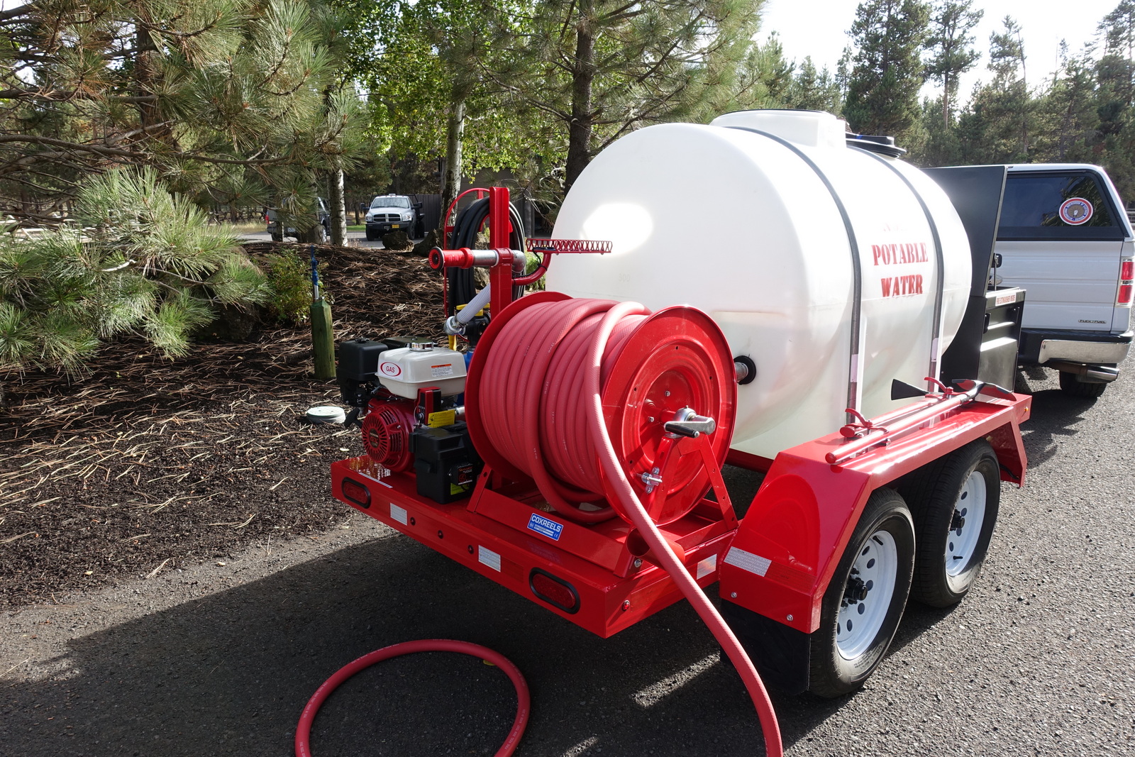 Red Trailer with white plastic water tank and multiple spigots and hoses.